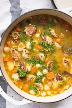 a large pot filled with meatball soup on top of a white table cloth next to a silver spoon