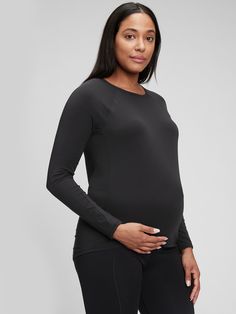 a pregnant woman wearing black pants and a long sleeved t - shirt, standing in front of a gray background