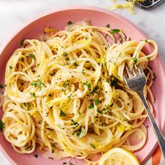 a pink plate topped with pasta and lemon wedges