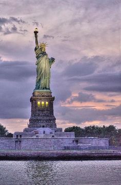 the statue of liberty is lit up at night with its lights on and water below