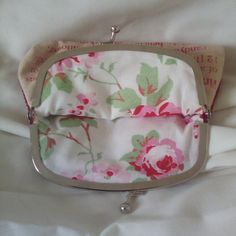 a small purse with flowers on it laying on a white bed sheet in front of a pillow