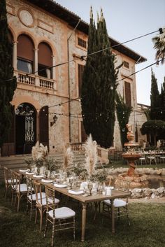 an outdoor dining area with tables and chairs in front of a large stone building surrounded by greenery