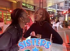 two women sitting at a table talking to each other in front of a sign that says sisters