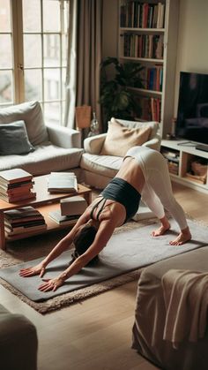 a woman is doing yoga in her living room with books on the floor and a couch