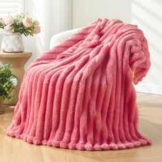 a pink blanket sitting on top of a wooden floor next to a vase with flowers