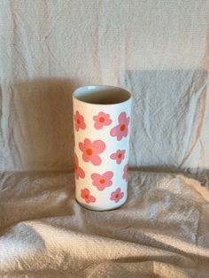 a white and pink flowered cup sitting on top of a bed covered in sheets