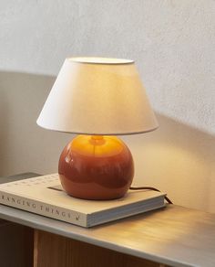 a lamp sitting on top of a wooden table next to a book with a white shade