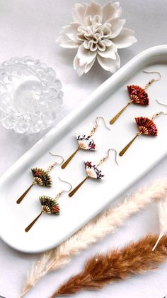 five different types of earrings on a white tray next to some feathers and a flower