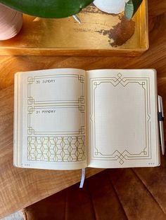 an open book sitting on top of a wooden table next to a pen and plant