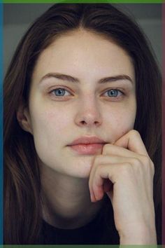 a woman with long brown hair and blue eyes is looking at the camera while she has her hand on her chin