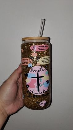 a hand holding a glittered cup with a straw in it that has a cross on it