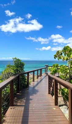 a wooden walkway leading to the ocean on a sunny day with blue sky and clouds