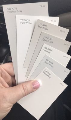 a person holding five different white paint samples in their hand, with the numbers on them