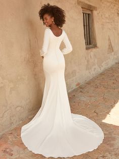 a woman in a white wedding dress leaning against a wall with her back to the camera