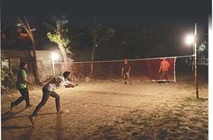 three people playing volleyball in the dark on a dirt field