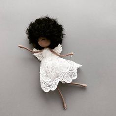 an angel doll with black hair and white wings on a gray background, laying down