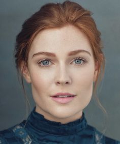 a woman with red hair and blue eyes is looking at the camera while wearing a blue dress