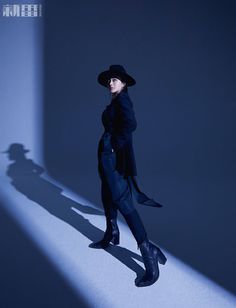 a woman in a black coat and hat standing next to a shadow on the wall