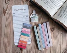 an open book next to some colored pencils on a wooden table with a pen and eraser