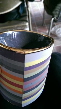 a hand holding a colorful striped cup on top of a table