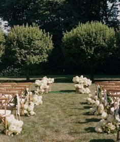 rows of wooden chairs with white flowers and greenery lining the aisle at an outdoor wedding ceremony