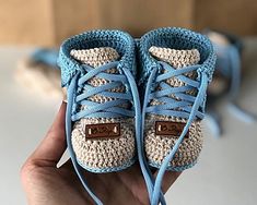 a hand holding up a pair of crocheted shoes with blue laces on them