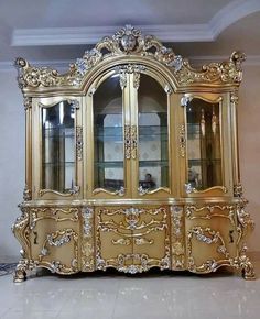 an ornately decorated gold china cabinet with glass doors on the front and side panels