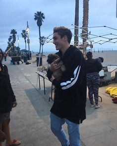 a man holding a small dog in his hands on the street next to palm trees