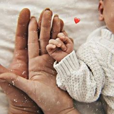 a person holding a baby's hand with a red heart on the top of it