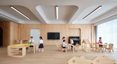 children are playing with wooden toys in the playroom, while adults sit at tables and chairs