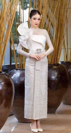 a woman standing in front of some vases wearing a white dress with an attached belt