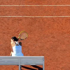 a woman sitting on a bench with a tennis racket in her hand and wearing a white tank top