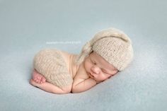 a newborn baby wearing a knitted hat and sleeping on a blue blanket with his eyes closed