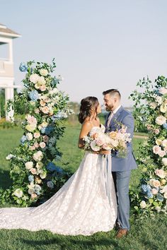 a bride and groom standing in front of an arch with flowers on it at their wedding