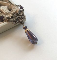 "Lovely and unique, here is an Art Nouveau teardrop necklace featuring a gorgeous translucent, purple glass teardrop bead which hangs from a stylish brass floral connector and is suspended from two tiny purple glass beads along with brass soldered chain for a truly unique vintage inspired piece! This necklace comes shipped in a special Botanical Bird gift box. All materials are lead and nickel safe. Handcrafted in the USA. Please choose your desired chain length from the drop down menu Jewel mea Wire Wrapped Teardrop Brass Necklaces, Antique Handmade Teardrop Necklace, Ornate Teardrop Necklace For Gift, Vintage Teardrop Drop Necklace, Vintage Handmade Teardrop Pendant Necklace, Bronze Teardrop Necklaces For Jewelry Making, Handmade Victorian Teardrop Jewelry, Vintage Dangle Drop Necklace For Gift, Elegant Czech Glass Drop Jewelry