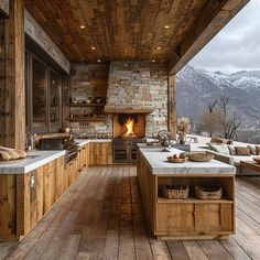 an outdoor kitchen and living room with wood flooring, stone fireplace and large windows