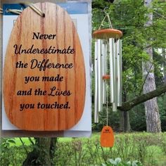 a wooden sign hanging from the side of a tree next to a wind chime