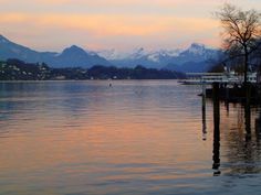 a body of water with mountains in the background and trees on both sides at sunset