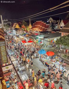 an aerial view of people walking around in the city at night with umbrellas and food stalls