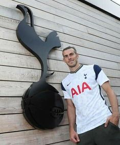 a man standing next to a wall with a basketball on it's back and a metal sculpture behind him