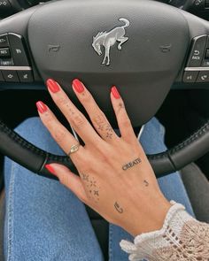 a woman's hand on the steering wheel of a car, with tattoos on her fingers