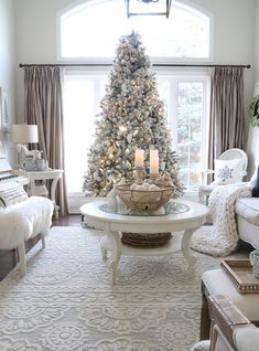 a living room decorated for christmas with a large tree in the corner and white furniture