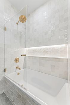 a bathroom with white tile and gold fixtures on the shower head, tub, and wall