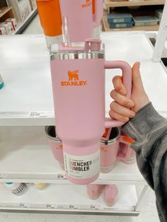 a person is holding a pink tumbler in their hand and it's on the shelf