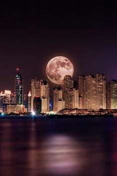 a full moon rises over the city skyline as seen from across the water at night