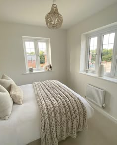 a bedroom with a bed, two windows and a chandelier hanging from the ceiling