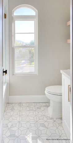 a white toilet sitting next to a window on top of a tiled floor in a bathroom