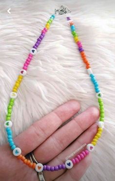 a hand holding a multicolored beaded necklace with an evil eye charm on it