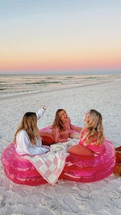 three women are sitting on an inflatable mattress at the beach and having a conversation