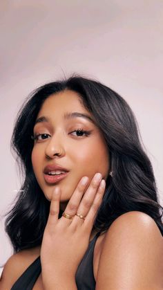 a woman with long black hair wearing a halter top and holding her hand to her face